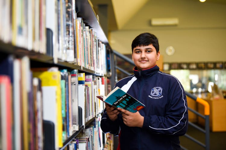 A student holding a book near a bookshelf in the library